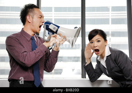 Businessman yelling through a megaphone at his colleague Stock Photo