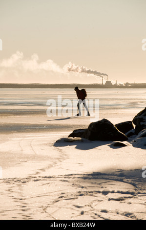 Silhouette of man skating on frozen lake, factory in background Stock Photo