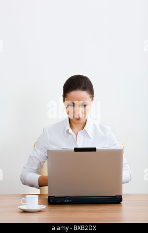 Isolated on white portrait of serious brunette businesswoman working on the laptop sitting at the table with a white cup on it Stock Photo