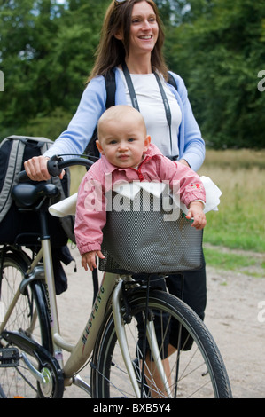 Mother pushing bicycle with baby in pannier Stock Photo