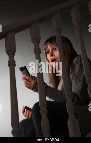 Shocked woman looking at her mobile phone, sitting on the stairs Stock Photo