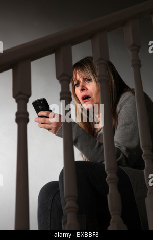 Shocked woman looking at her mobile phone, sitting on the stairs Stock Photo
