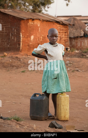 A young girl in a torn dress stands with jerry cans in Igamba village, Iganga District, Eastern Uganda, East Africa. Stock Photo