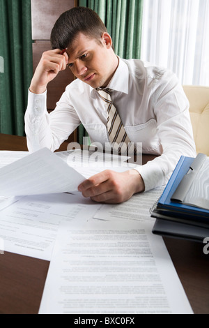 Thinking businessman touching his head holding a document sitting at the table Stock Photo