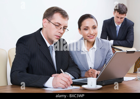 Portrait of young businesswoman looking at the monitor of laptop placed on the table with papers and cup of coffee on it and bus Stock Photo