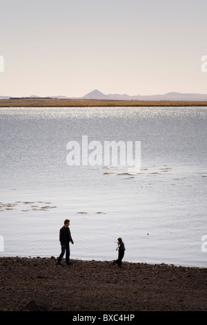 Boy throwing rocks into the ocean, his father standing by. Reykjavik Iceland Stock Photo