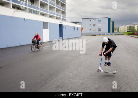 Boy jumping on a scooter outside apartment blocks. Hafnarfjordur, Greater Reykjavik Area, Iceland Stock Photo