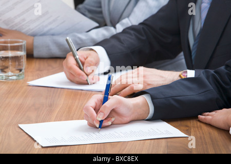 Human hands holding pens and papers, making notes in documents on the table with glasses of water on it Stock Photo