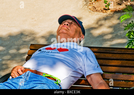 Mature Asian man taking power nap on park bench in middle of day Stock Photo