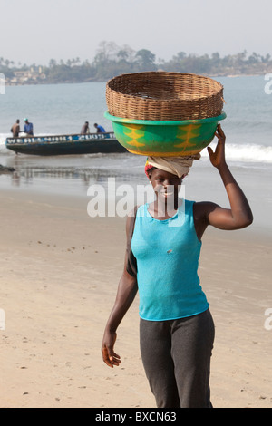 A woman stands with a basket on her head on the beaches of Freetown, Sierra Leone, West Africa. Stock Photo