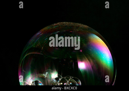 A close up of a soap bubble reflecting a rainbow of light on a black background. Stock Photo