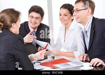 Group of four young businesspeople discussing different questions gathered together around the table with the laptop, drinks and Stock Photo