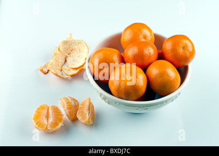 Peeled clementines and clementines in white bowl on white surface Stock Photo