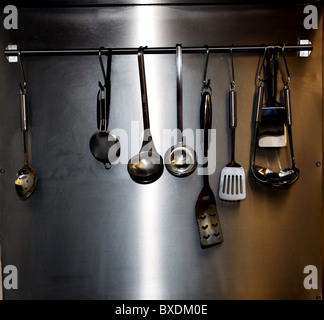 Cooking utensils hanging on rail in commercial kitchen Stock Photo - Alamy