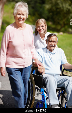Two women walking with man in a wheelchair Stock Photo