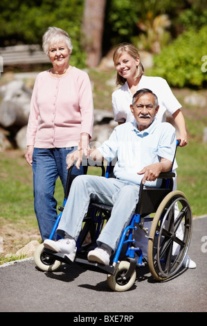 Two women walking with man in a wheelchair Stock Photo