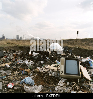 Burned rubbish and a television dumped on waste ground looking towards Redcar Steelworks. Stock Photo