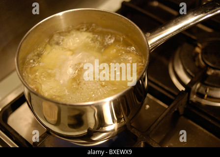 Potatoes simmering in a pan of boiling water on a gas hob. Stock Photo