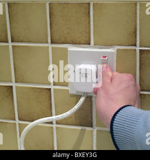 Caucasian Man Switching ON/Off Electricity Supply at a Wall Socket with a Three Pin Fused Plug Plugged In, UK MODEL RELEASED Stock Photo