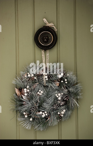 A Christmas wreath hands from a brass door knocker on a green door. Stock Photo