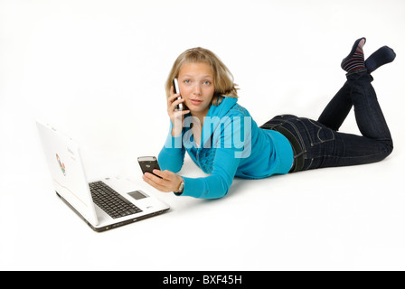 Young woman, 21 years, lying on the ground with a laptop computer and two telephones. Stock Photo