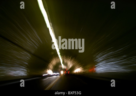 Car speeding through a tunnel with head lights and tail lights reflecting off  dome and sides of the tunnel Stock Photo