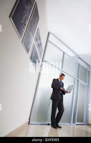 Business man is standing in the corridor, holding the laptop Stock Photo