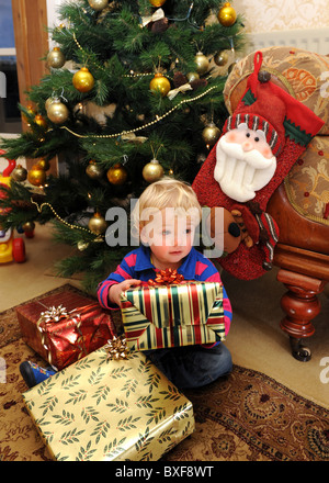Baby boy opening Christmas presents in front of Xmas tree Stock Photo