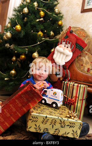 Baby boy opening Christmas presents in front of Xmas tree Stock Photo