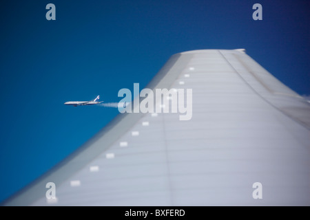 Passenger jet aircraft viewed across plane wing from porthole of another in flight on route to America Stock Photo