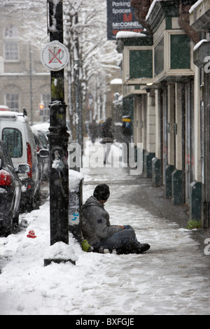 street beggar sitting in the snow on a cold snowy winters day Belfast Northern Ireland Stock Photo