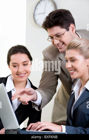 Boss is explaining the correct way of analysis to his colleagues in the office pointing at the monitor Stock Photo