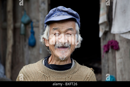An old man outside his rustic and squalid wooden home in an isolated mountain village in Gansu province in China. Stock Photo