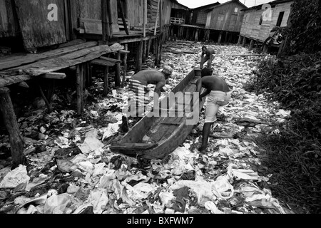 Displaced boys push the canoe over the garbage patch in the stilt house area in Tumaco, Nariño dept., Colombia. Stock Photo