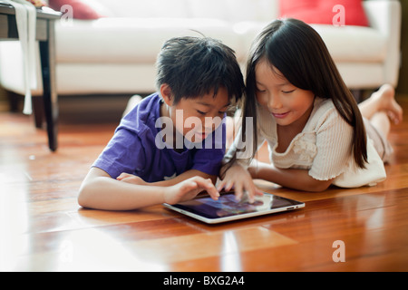 Mixed race brother and sister using digital tablet on floor Stock Photo