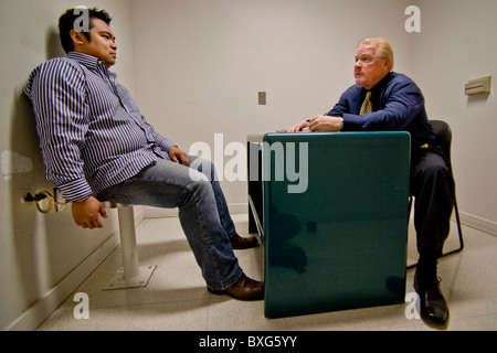 A handcuffed felony suspect is questioned by a Santa Ana, CA, police detective in a specialized interrogation room. Stock Photo
