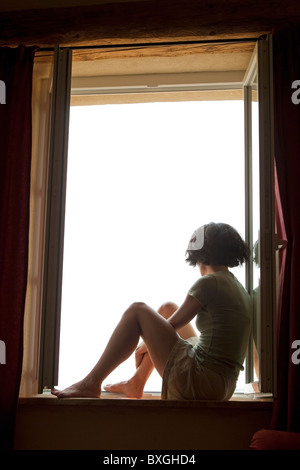 Woman sitting on window ledge and thinking looking out of a window