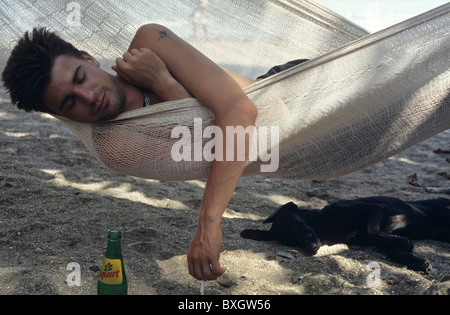 Costa Rica, young man in Montezuma snoozing in hammock with cigarette in hand, black little dog sleeping in shadow, soft drink Stock Photo