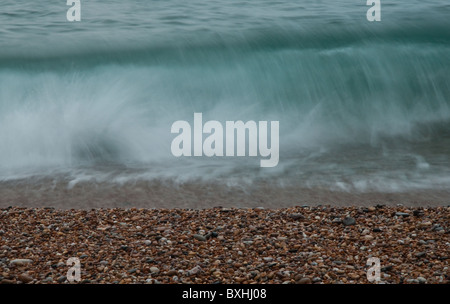 A long exposure shot of a wave breaking on a shingle beach. Stock Photo