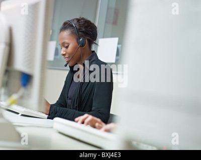 female african american customer service representative talking on the phone and typing on pc. Horizontal shape, side view, copy Stock Photo