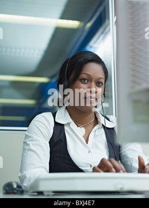 female african american customer service representative talking on the phone and typing on pc. Vertical shape, front view Stock Photo