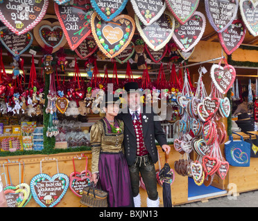 A couple in traditional dress in front of a 'Gingerbread hearts' stall at Oktoberfest, Munich, Germany Stock Photo