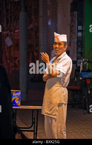 Asian male kitchen worker standing outside of restaurant smoking a cigarette in downtown Hong Kong China Stock Photo