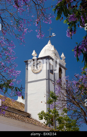 Moncarapacho Village Church Clock Tower And Jacaranda Tree In Flower, the Algarve Stock Photo