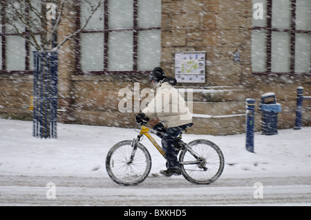 Cyclist riding during heavy snowfall, Warwick town centre, UK Stock Photo