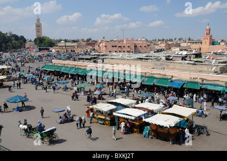 View across busy Djemaa el-Fna meeting place to the Mosque on the right and a distant view of Kotoubia Mosque Stock Photo