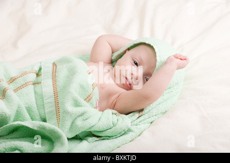 Ten weeks old cute little baby girl wrapped in towel stretching in bed Stock Photo