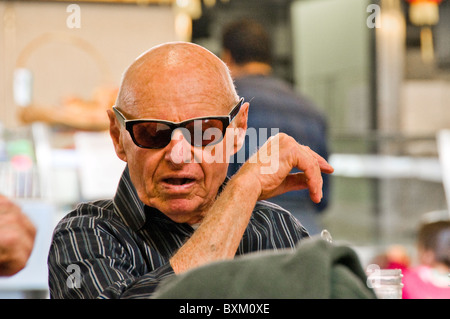 Older Caucasian man sitting down at empty table in restaurant at Farmers market Los Angeles Stock Photo