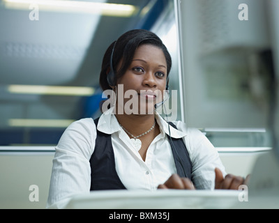 female african american customer service representative talking on the phone and typing on pc. Horizontal shape, front view Stock Photo