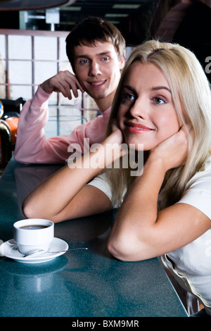 Smiling cute blond woman drinking coffee in the bar and handsome brunette man behind admiring her Stock Photo